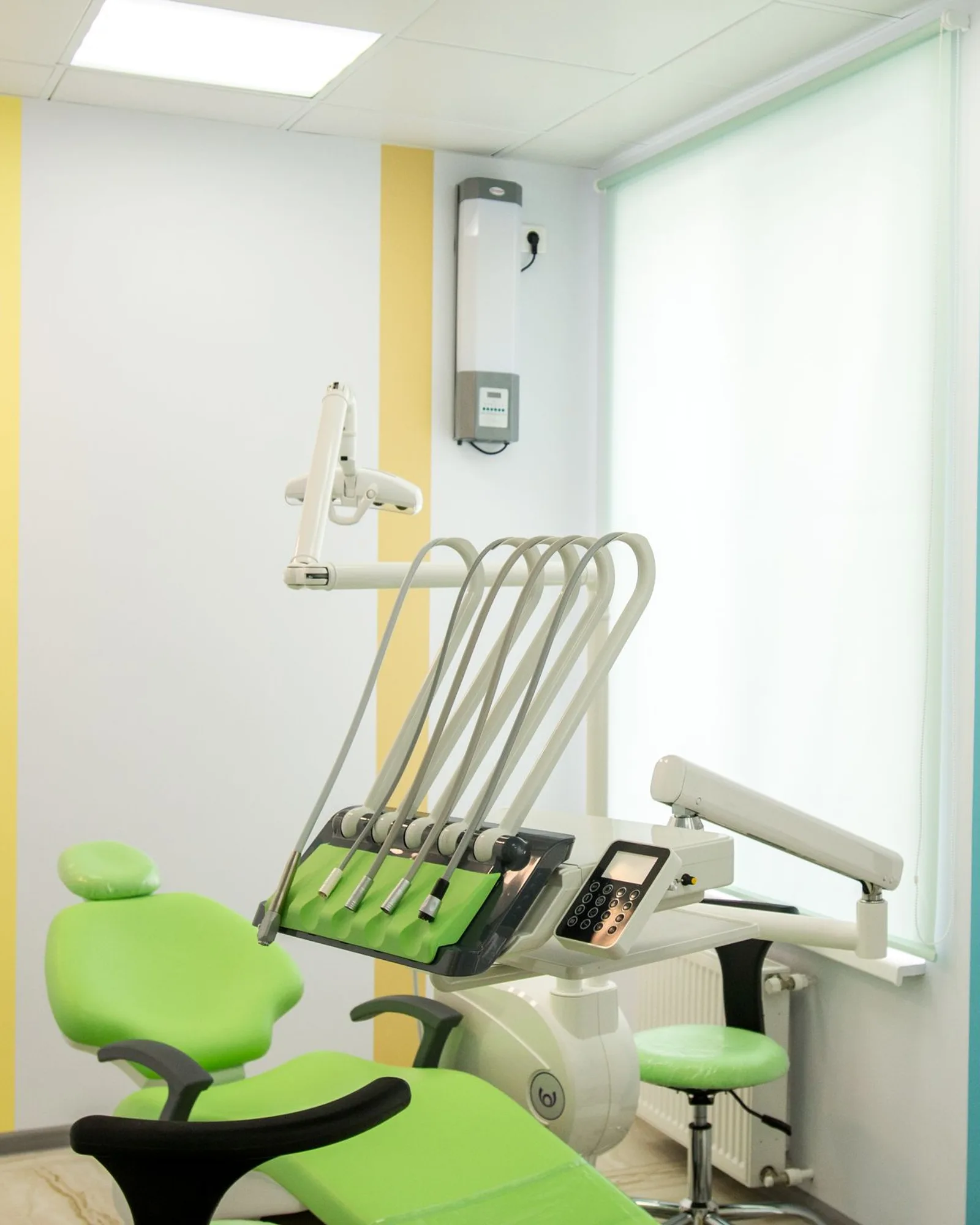 A pediatric dental treatment room with a child-sized green chair beside a bright, daylit window.