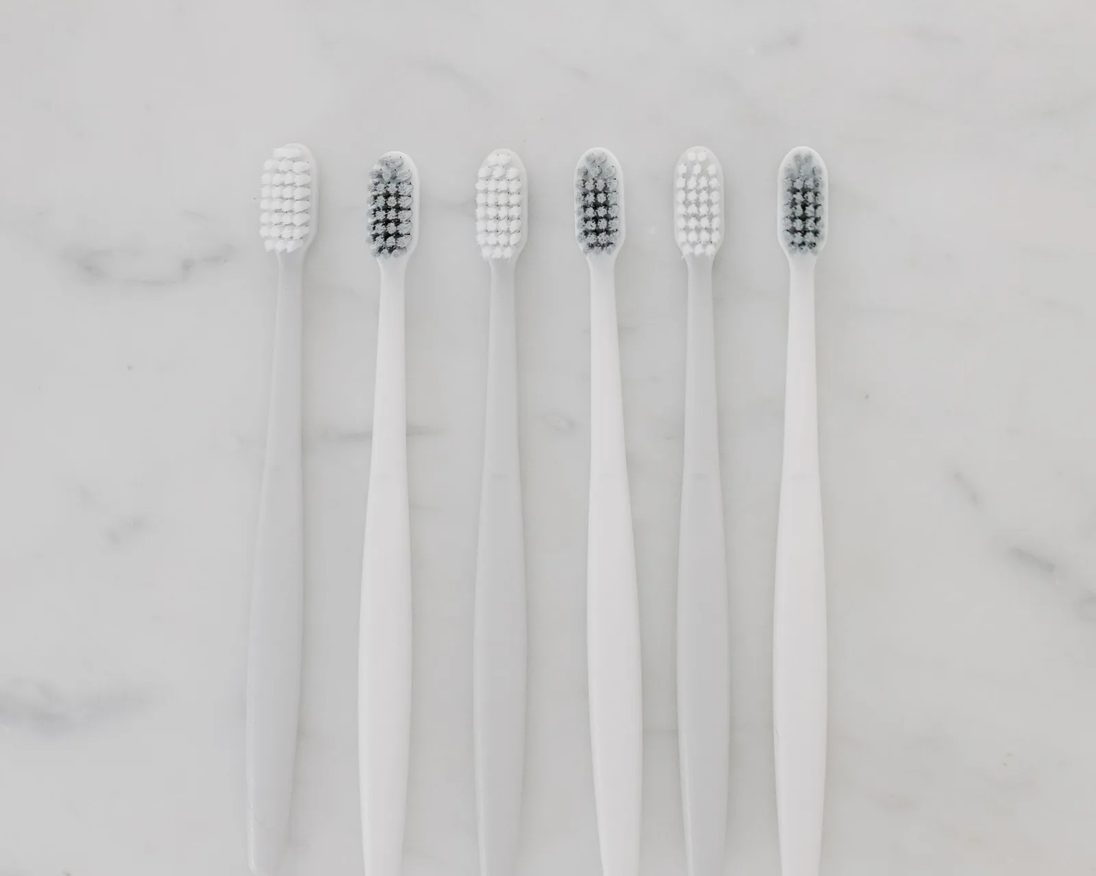 Six toothbrushes laid in a row on a pale marble surface.