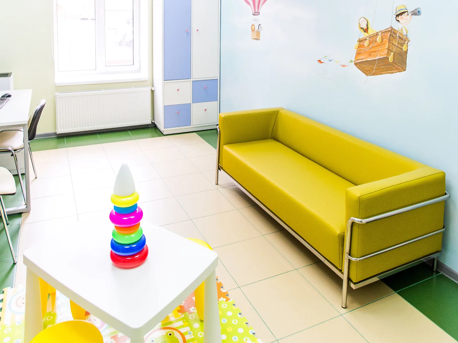A colourful, child-scaled room with soft seating and toys, sized for a young patient.